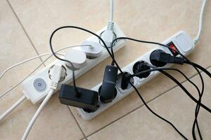 Overloaded power boards. Power strips with different electrical plugs on white floor photo