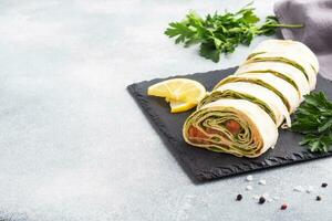 Rolls of thin pita bread and red salted salmon with lettuce leaves On a slate stand, grey concrete background. Copy space. photo