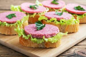 Sandwiches with lettuce leaves and sliced salami sausage on a wooden Board. photo