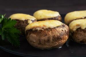 Baked mushrooms stuffed with cheese and herbs on a black plate. wooden background. photo