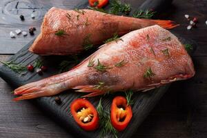 Raw fish perch without a head with lemon slices and dill greens and red chili peppers on wooden cutting Board with dark rustic background. Healthy food and diet concept. Ingredients for cooking fish photo