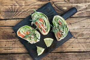 Rolls of thin pita bread and red salted salmon with lettuce leaves on a wooden cutting Board. Copy space. photo