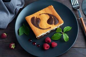 A piece of double-layer cake on a plate of chocolate brownies and curd cheesecake with raspberries. Dark background copy space photo