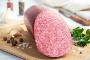 A loaf of salami Servelat sausage on a cutting Board with parsley and spices and garlic. photo