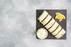 Rolls of thin pita bread and red salted salmon with lettuce leaves On a slate stand, grey concrete background. Copy space. photo