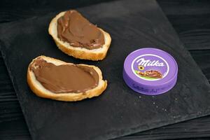 KHARKOV, UKRAINE - JULY 2, 2021 Milka sweetened hazelnut cocoa spread with classical lilac color design on black table photo