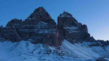 Tre Cime Di Lavaredo. The Three Peaks at Morning Twilight in Winter and Auronzo Hut. Blue Hour. Aerial View. Sexten Dolomites, South Tyrol. Italy. Orbiting. View from the South video