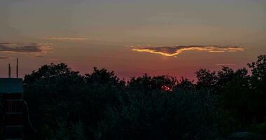 Time-lapse video of a sunset over land with fast-moving clouds and bushes in the foreground