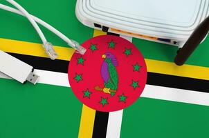 Dominica flag depicted on table with internet rj45 cable, wireless usb wifi adapter and router. Internet connection concept photo