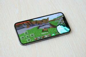Minecraft mobile iOS game on iPhone 15 smartphone screen on wooden table during mobile gameplay photo