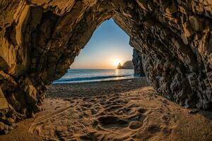 view from the stone cave on the sunset sea and the beach, the volcanic rock of the cave is lit by the warm setting sun photo