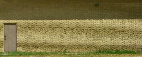 Texture of brick wall from relief stones under bright sunlight with metal door photo