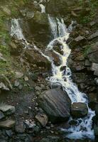 A mountain waterfall flows over the rocks. Waterfall cascade on mossy rocks photo