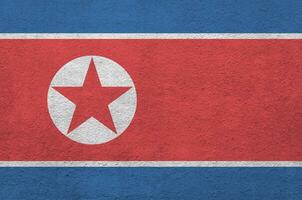 North Korea flag depicted in bright paint colors on old relief plastering wall. Textured banner on rough background photo