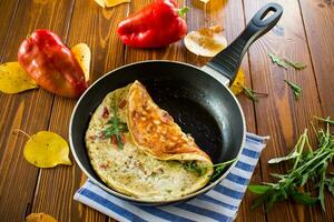 Fried omelets with various autumn vegetables in a frying pan on a wooden table. photo