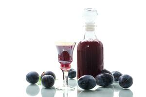 plum red wine in a glass and a decanter against the background of ripe large plums photo