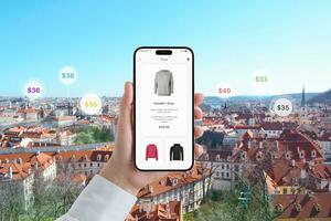 teléfono en mano muestra un compras aplicación con un sudadera. precios en el fondo de ciudad paisaje foto