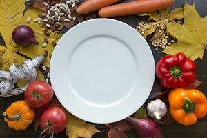 Autumn background with various vegetables around white empty dish with top view photo