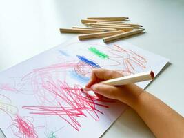 pequeño niño sorteos con de colores lapices en papel en blanco mesa. foto