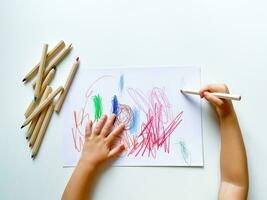 small child draws with colored pencils on paper on white table. photo