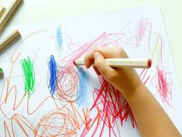 pequeño niño sorteos con de colores lapices en papel en blanco mesa. foto