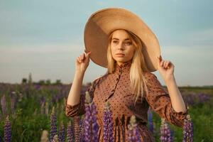 A beautiful woman in a straw hat walks in a field with purple flowers. A walk in nature in the lupin field photo