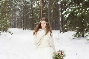 hermosa novia en un blanco vestir con un ramo de flores en un cubierto de nieve invierno bosque. retrato de el novia en naturaleza foto