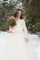 Beautiful bride in a white dress with a bouquet in a snow-covered winter forest. Portrait of the bride in nature photo