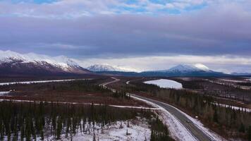 Car on Parks Highway and Snow-Capped Mountains on Cloudy Winter Day. Landscape of Alaska, USA. Aerial View. Drone Flies Forward video