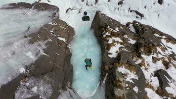 hielo alpinismo en congelado cascada. alpinista mujer es líder en hielo. aéreo De arriba hacia abajo vista. bareskoon valle, Kirguistán. zumbido moscas hacia arriba video