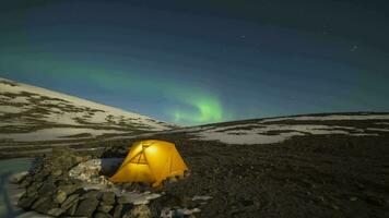 natt starry himmel och grön nordlig lampor över lysande gul tält i khibiny bergen på vinter- natt. Ryssland. tid upphöra video