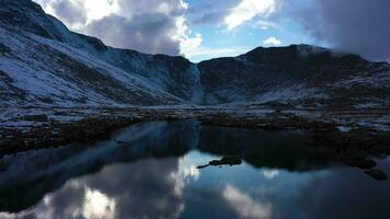 cumbre lago parque en montar evans área. Nevado montañas reflexión en lago y nublado cielo. aéreo vista. Colorado, EE.UU. zumbido moscas adelante a bajo nivel terminado lago video