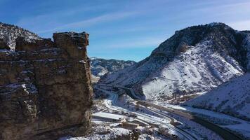 Castle Gate Spire on Sunny Winter Day. Snowy Mountains and Road. Utah, USA. Aerial View. Drone Flies Forward and Upwards video