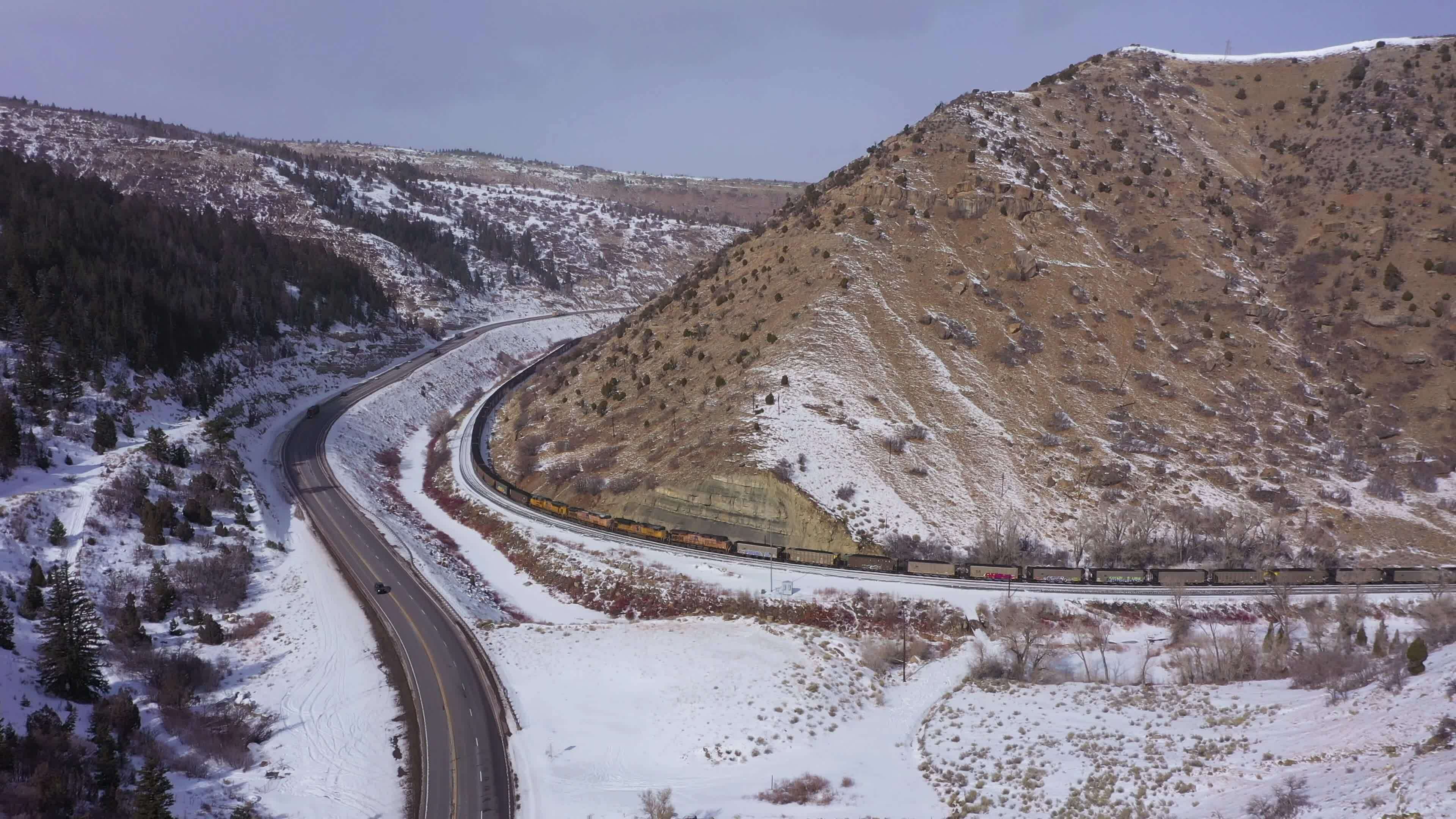 Freight Train, Highway and Snowy Mountains on Sunny Winter Day. Snowing. Utah, USA. Aerial View