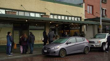 Seattle, Verenigde Staten van Amerika - februari 4, 2021 mensen vervelend maskers zijn bekleed omhoog Aan trottoir en praktijk sociaal afstand nemen aan het wachten naar invoeren de eerste Starbucks op te slaan gedurende coronavirus pandemie. snoek plaats video