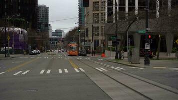 Seattle, Stati Uniti d'America - febbraio 4, 2021 tram, strada e paesaggio urbano su inverno nuvoloso giorno. persone indossare maschere attraversamento un' strada durante coronavirus pandemia. auto traffico video