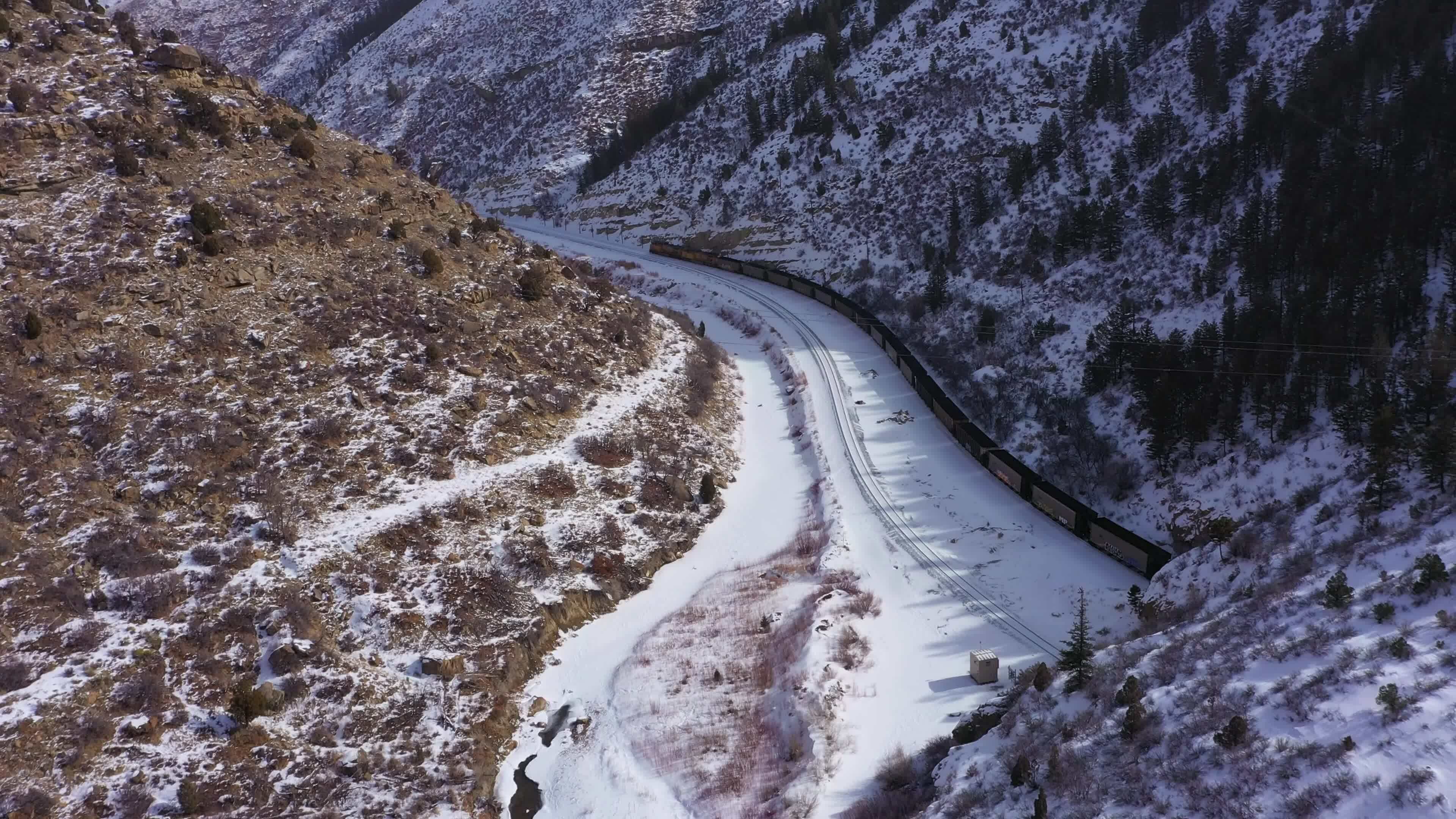 Freight Train and Snowy Mountains on Sunny Winter Day. Snowing. Utah, USA. Aerial View. Drone