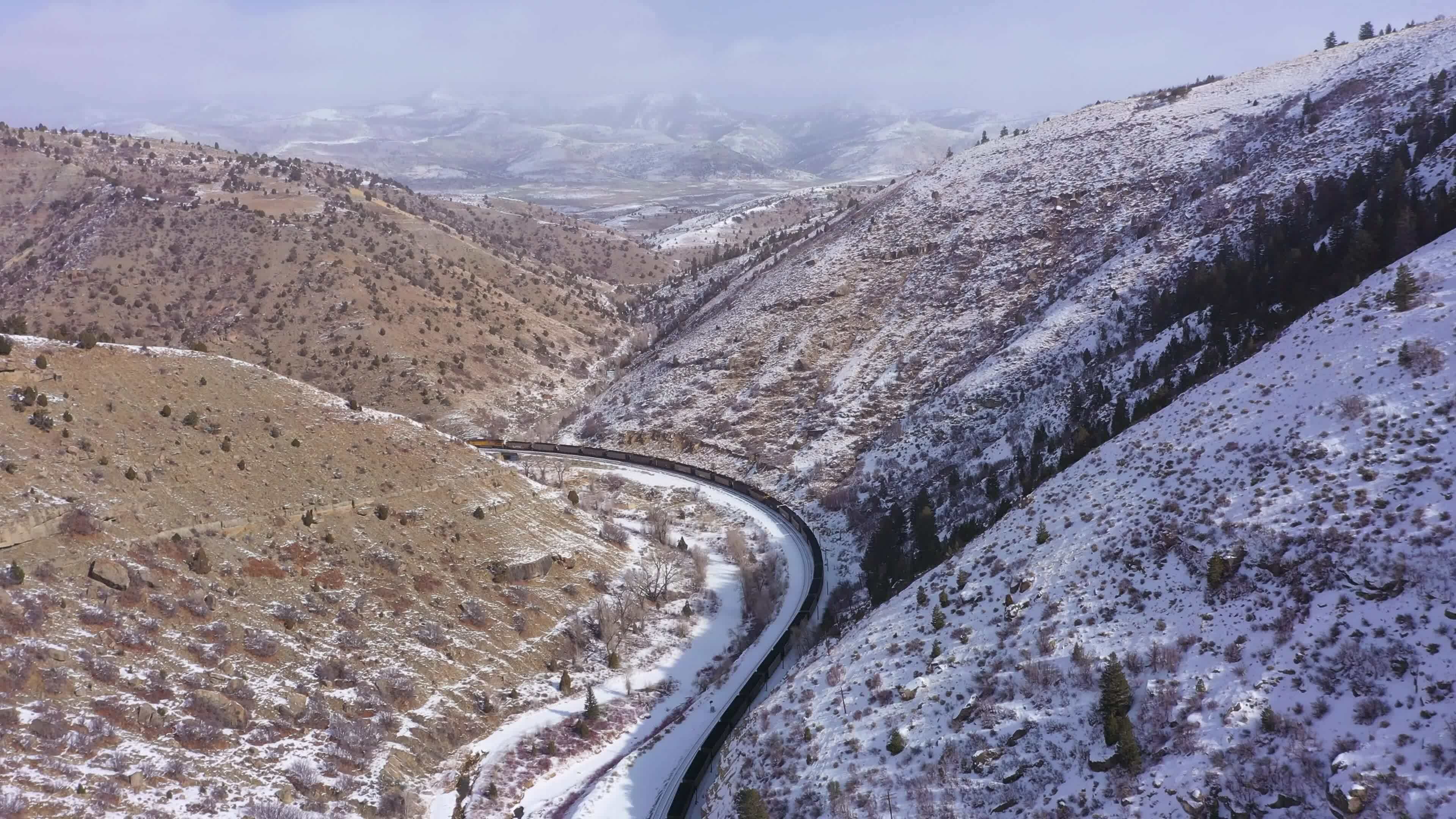 Freight Train and Snowy Mountains on Sunny Winter Day. Snowing. Utah, USA. Aerial View. Drone