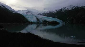 Portage Glacier, Portage Lake, Reflection and Snow-Capped Mountains on Sunny Day. Alaska, USA. Aerial View. Drone Flies Backwards and Upwards video