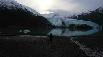 man promenader mot portage glaciär. portage sjö, reflexion och snötäckt bergen på solig dag. alaska, usa. antenn se video