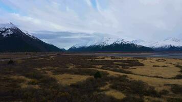 Red Bushes and Snow-Capped Mountains on Autumn Day. Landscape of Alaska, USA. Aerial View. Drone Flies Backwards and Upwards video