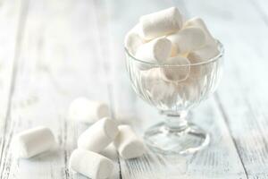 Glass bowl of marshmallows on the wooden background photo