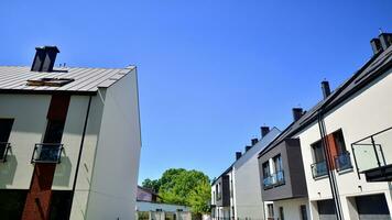 Suburban neighborhood with condominium complex. Suburban area with modern geometric family houses. Row of family houses against blue sky. photo