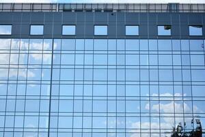 Glass building with transparent facade of the building and blue sky. Structural glass wall reflecting blue sky. Abstract modern architecture fragment. Contemporary architectural background. photo