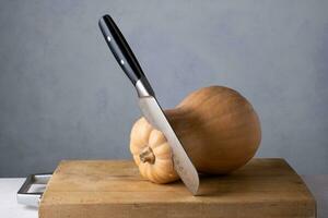 Ripe pumpkin and a large kitchen knife on a wooden cutting board. photo