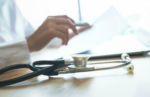 Stethoscope on desk and doctor using laptop with looking in medical journal. photo