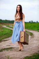 Pretty woman travels on the road in the field. Girl with with a big suitcase photo