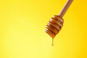 Fresh honey pouring from a wooden spoon yellow background photo