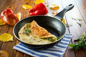 Fried omelets with various autumn vegetables in a frying pan on a wooden table. photo