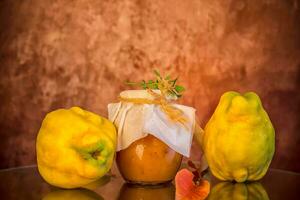 Ripe quince fruits with jam in a glass jar on a dark wooden table. photo